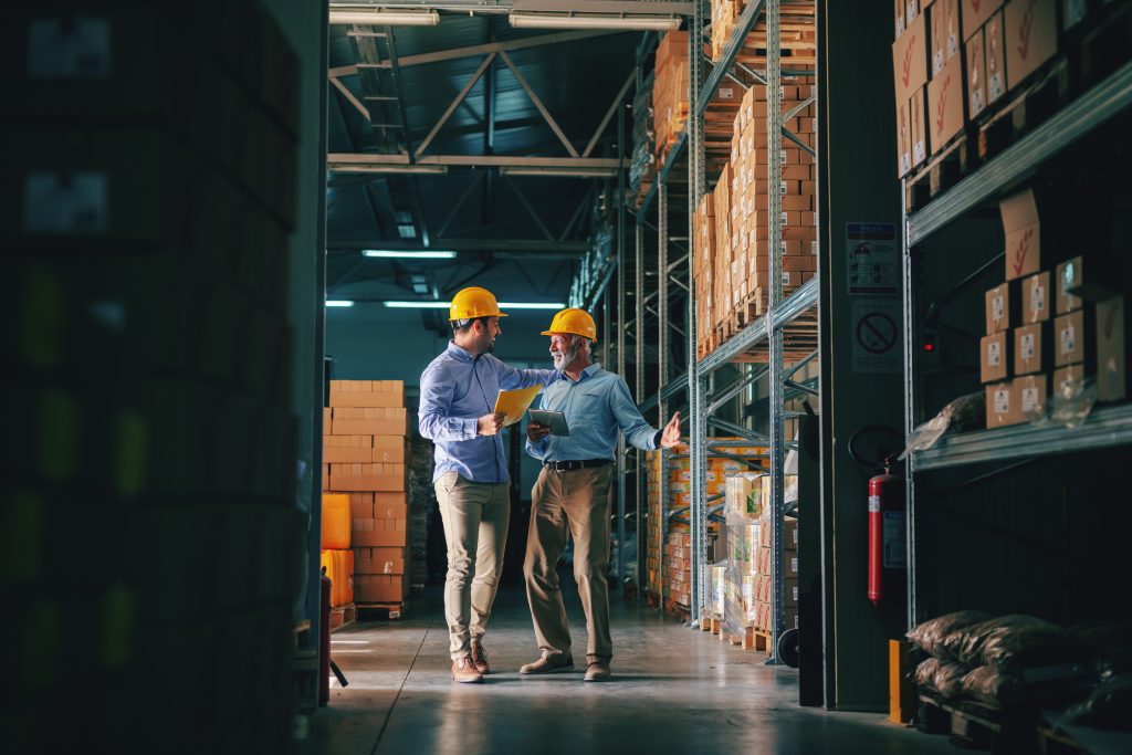 Two successful business partners in formal wear discussing about sales while standing in warehouse.